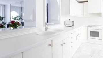 A modern, white bathroom with a large mirror, two sinks, a toilet, and a shower.