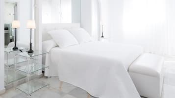 Een moderne slaapkamer met een groot bed, glazen nachtkastjes en een spiegel.