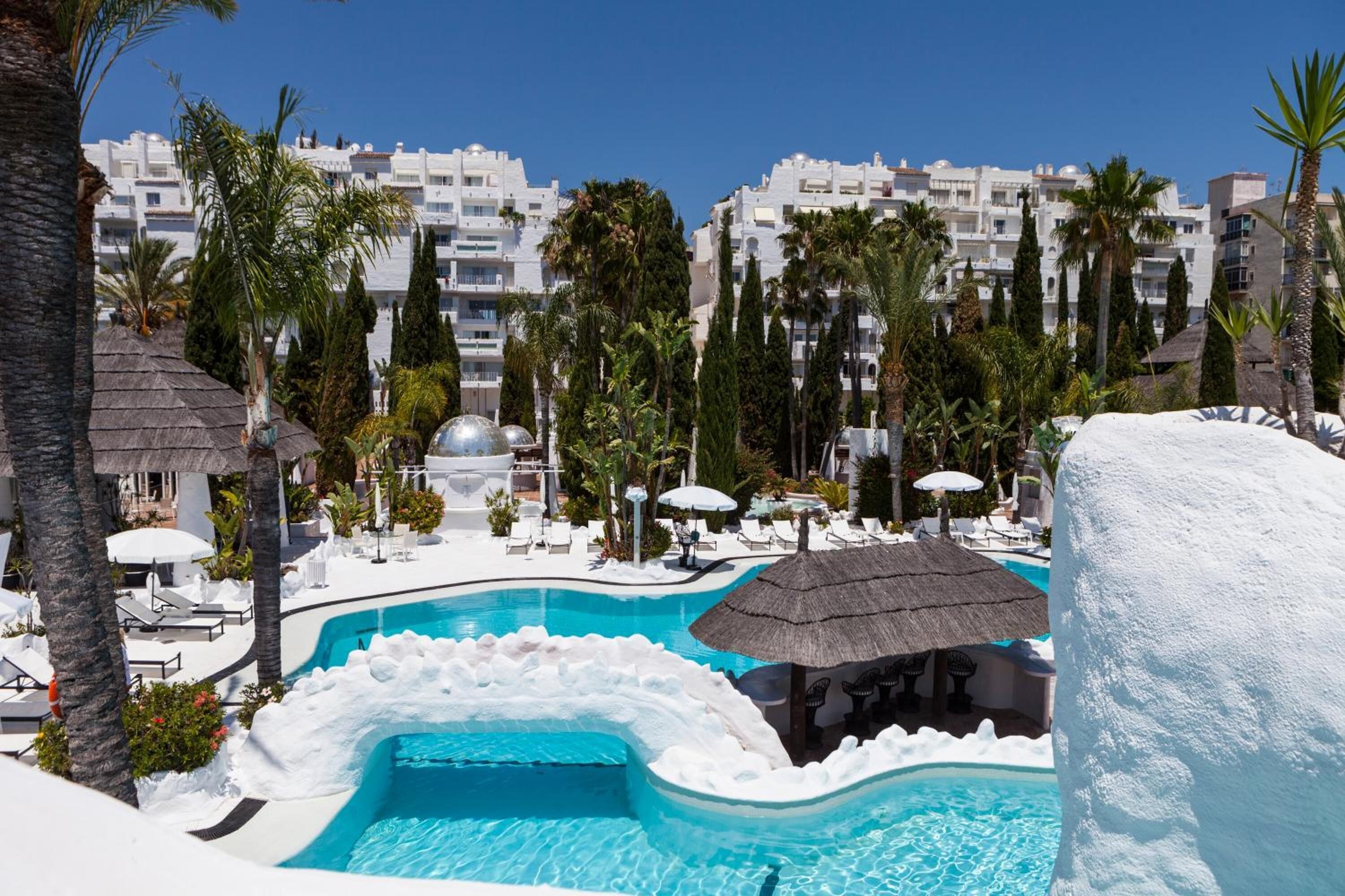 A resort pool with a white, icy edge, surrounded by palm trees and lounge chairs.