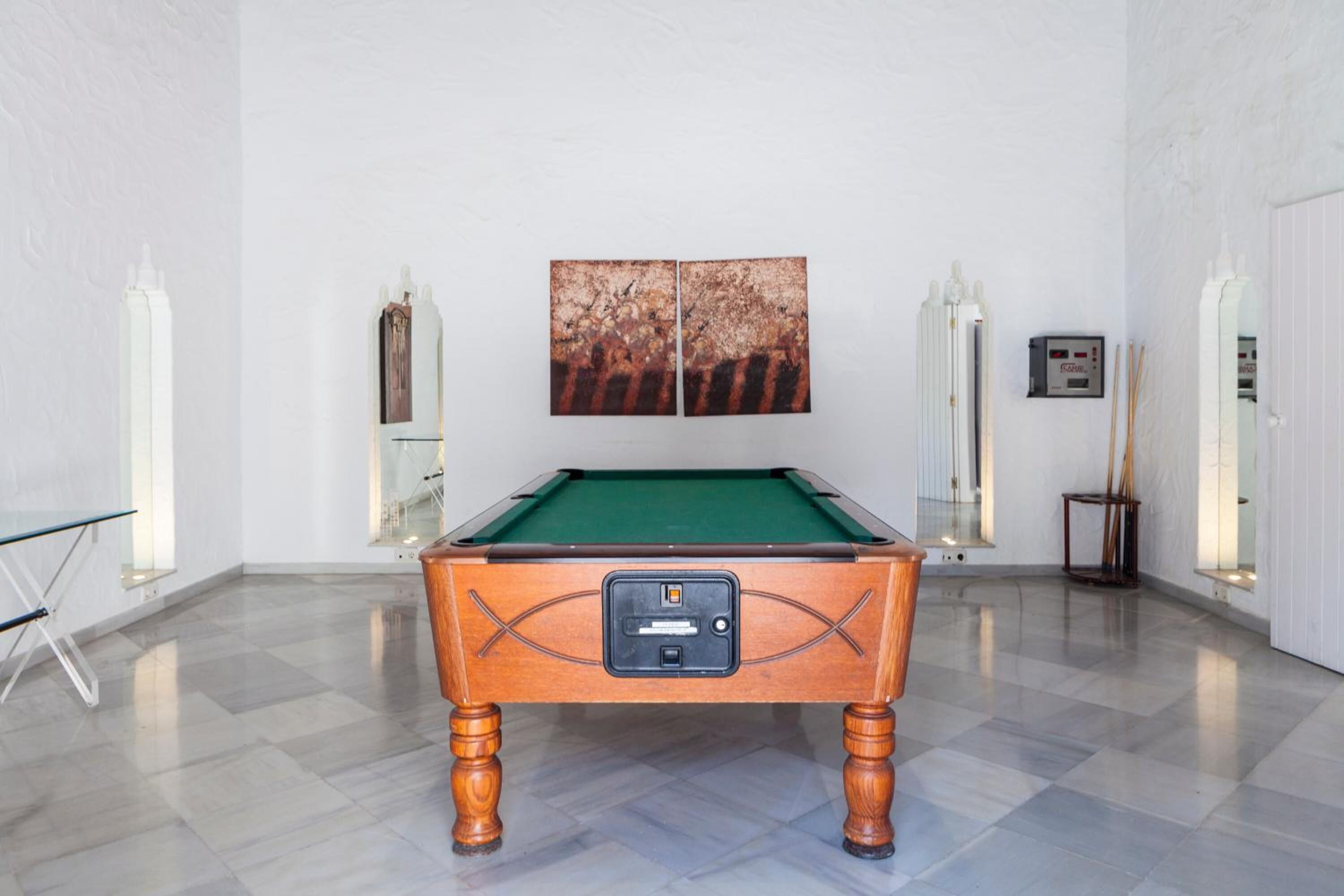 A pool table in a room with a tiled floor, white walls, and a painting above it.