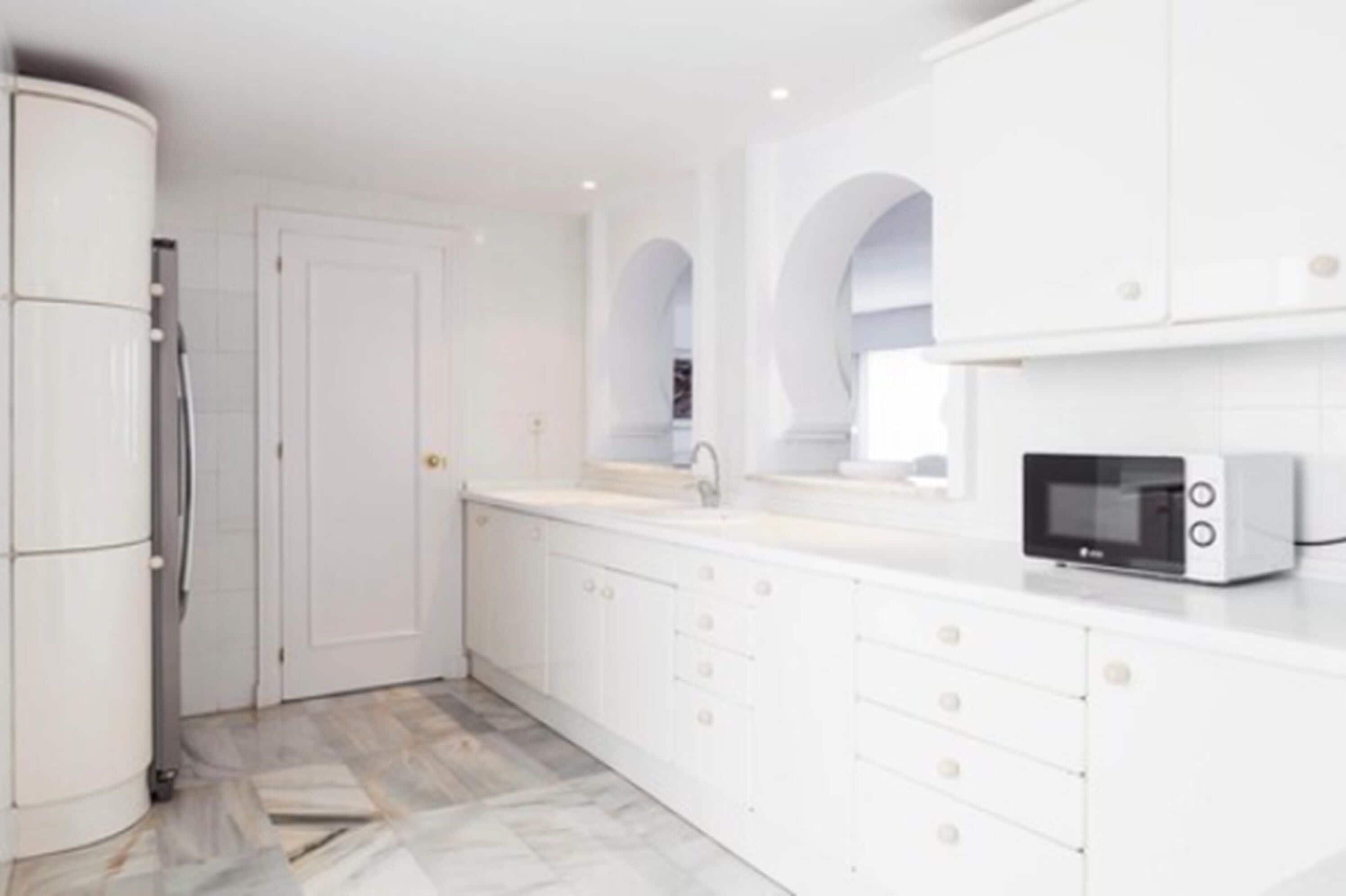 A modern kitchen with white cabinetry, a built-in microwave, and a refrigerator.