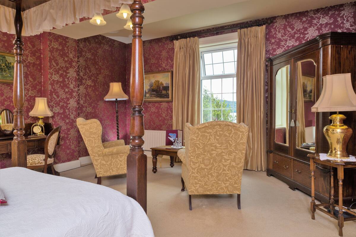 A room with a large bed, two armchairs, a wooden cabinet, and a window with curtains.