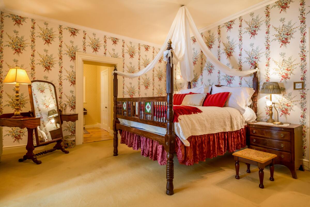 A four-poster bed with a canopy, a wooden nightstand, a mirror, and a small bench.