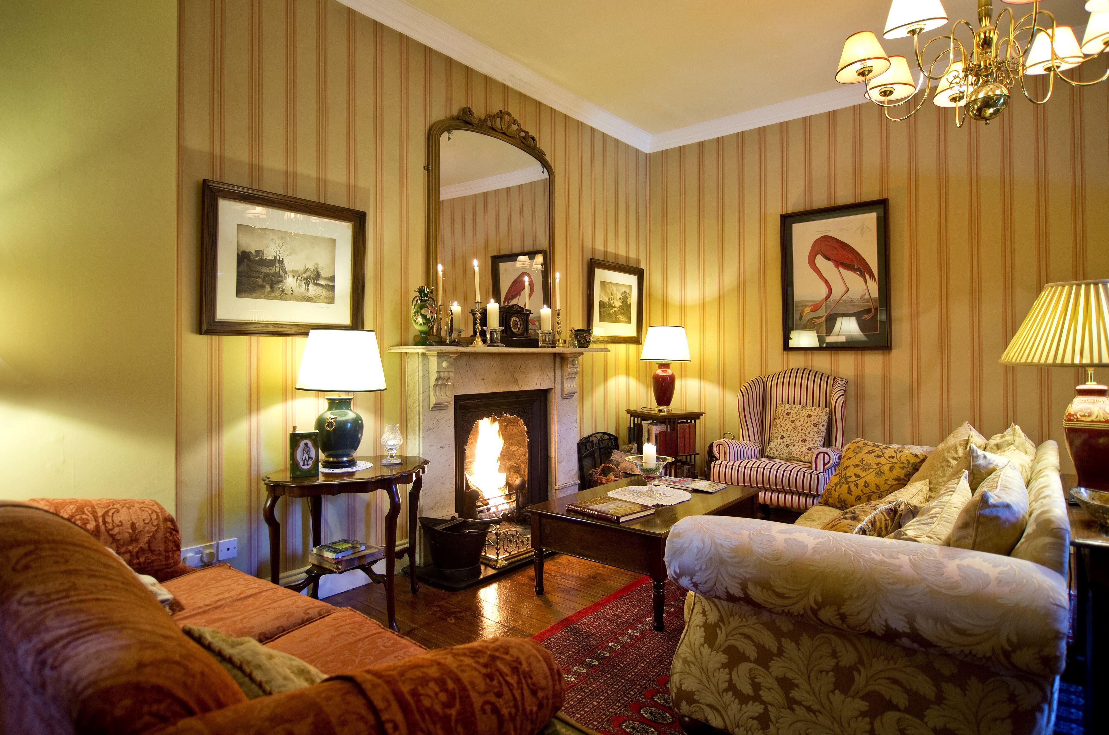 A cozy living room with striped wallpaper, a fireplace, a chandelier, and comfortable seating.