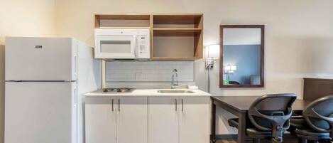 A compact kitchen with a refrigerator, microwave, sink, and wooden cabinets.