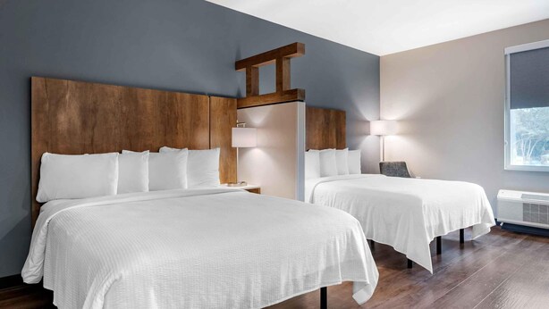 Habitació d'hotel amb dos llits, un panell de fusta al capçal, una meseta de nit amb una làmpada i una finestra gran.