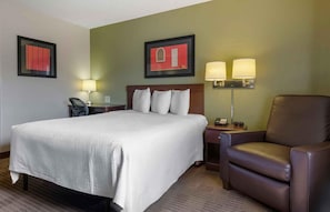 Habitación de hotel con una cama grande, un sillón de cuero marrón, dos lámparas fijadas a la pared y obras de arte enmarcadas.