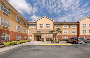 A multi-story hotel with a central lobby entrance, marked by a sign. - Extended Stay America Suites Orlando Lake Mary 1036 Greenwoo (Lake Mary)