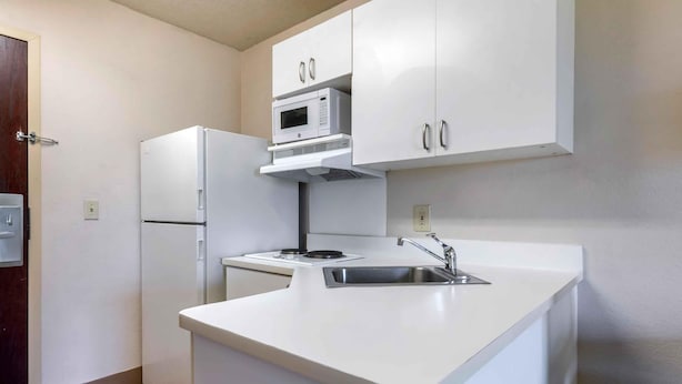 Une cuisine compacte avec des meubles blancs, un four à micro-ondes encastré, un réfrigérateur et un évier.