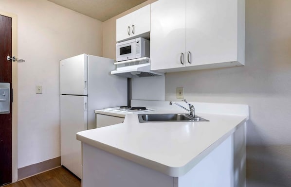 Una cocina compacta con armarios blancos, un microondas integrado, un refrigerador y un lavamanos.