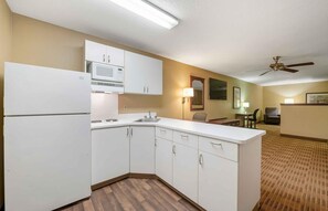 A compact kitchen with white cabinets, a microwave, and a refrigerator. There is a dining area with a table and chairs, and a ceiling fan. - Extended Stay America Suites Orlando Lake Mary 1036 Greenwoo (Lake Mary)