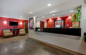 A reception area with a red wall, a black reception desk, two beige armchairs, a flat-screen TV, and a potted plant. - Extended Stay America Suites Orlando Lake Mary 1036 Greenwoo (Lake Mary)
