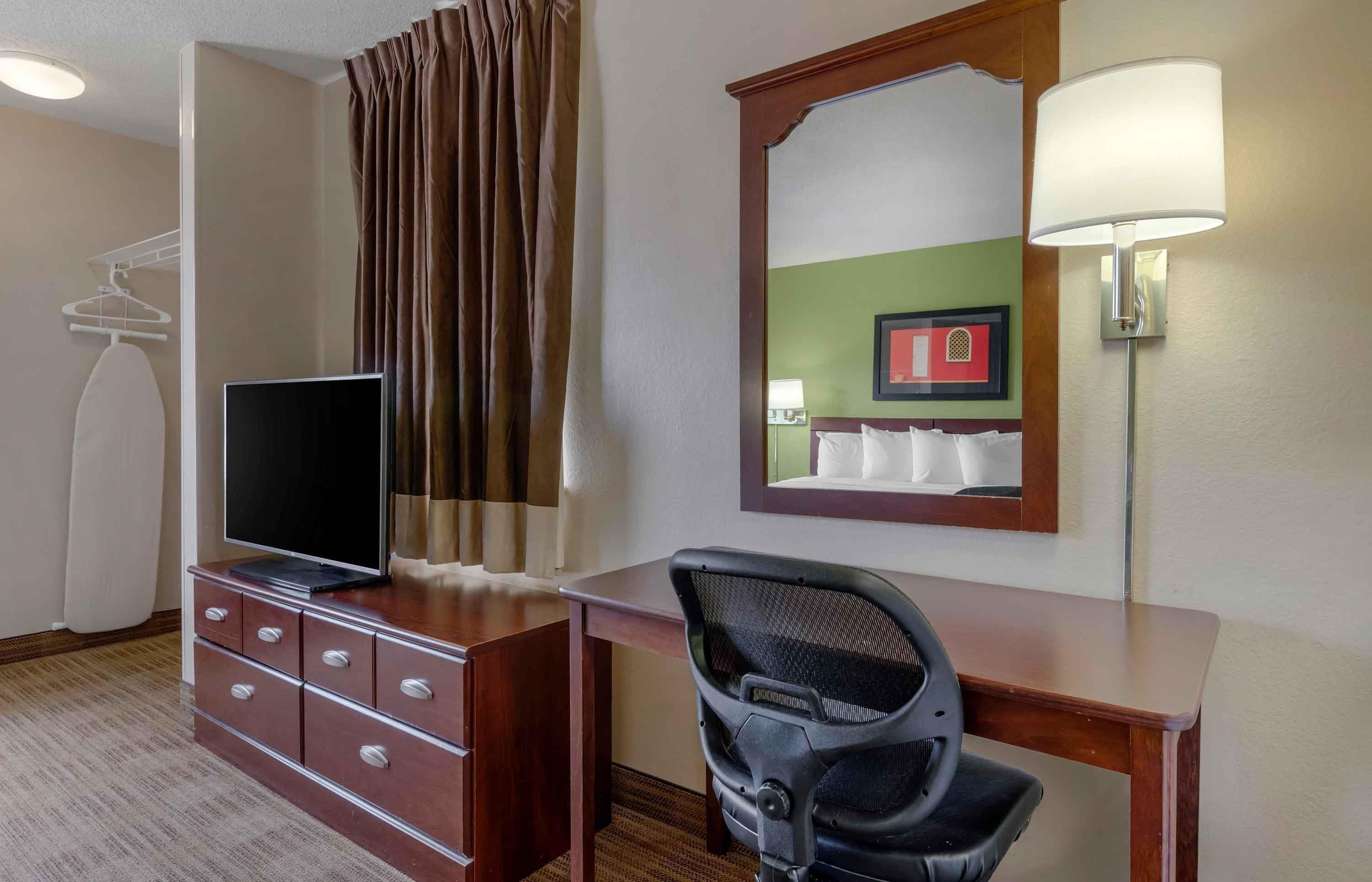 Une chambre d’hôtel équipée d’un téléviseur à écran plat posé sur une commode, d’un bureau avec une chaise, d’une lampe et d’un miroir.