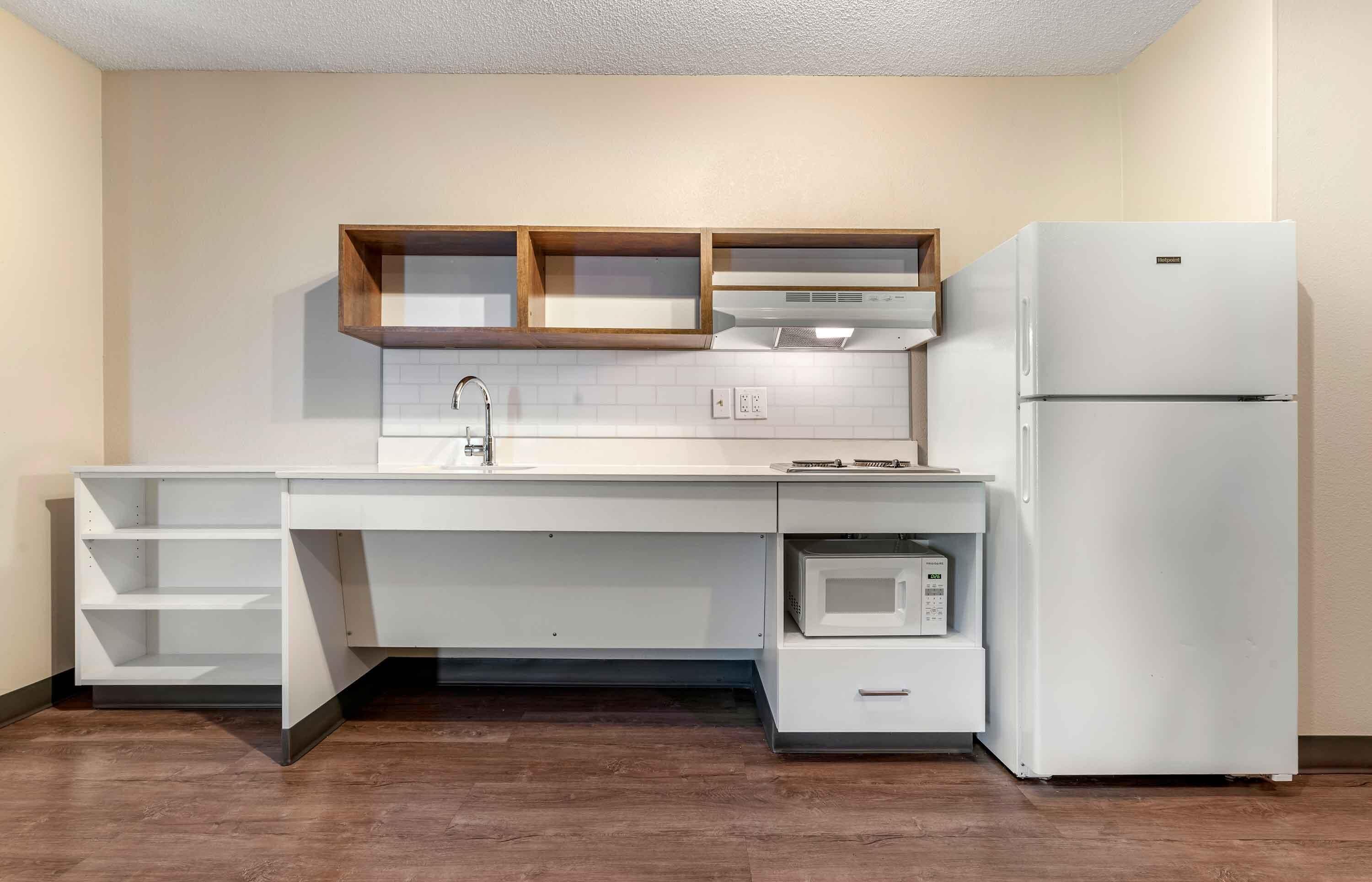 A compact kitchen with white cabinetry, a built-in microwave, and a refrigerator.