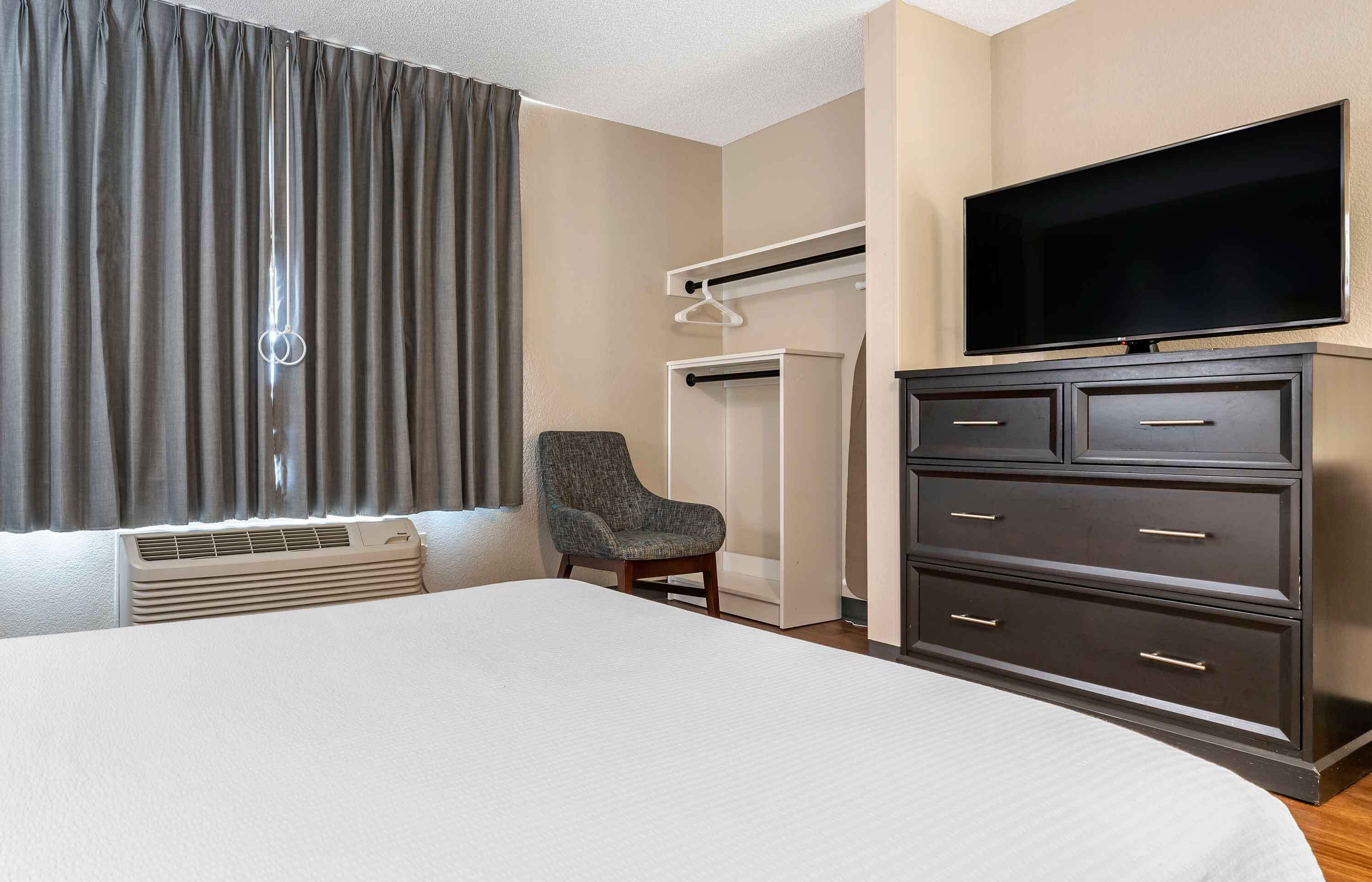 A hotel room with a large bed, a chair, a wardrobe, a television, and a window with curtains.