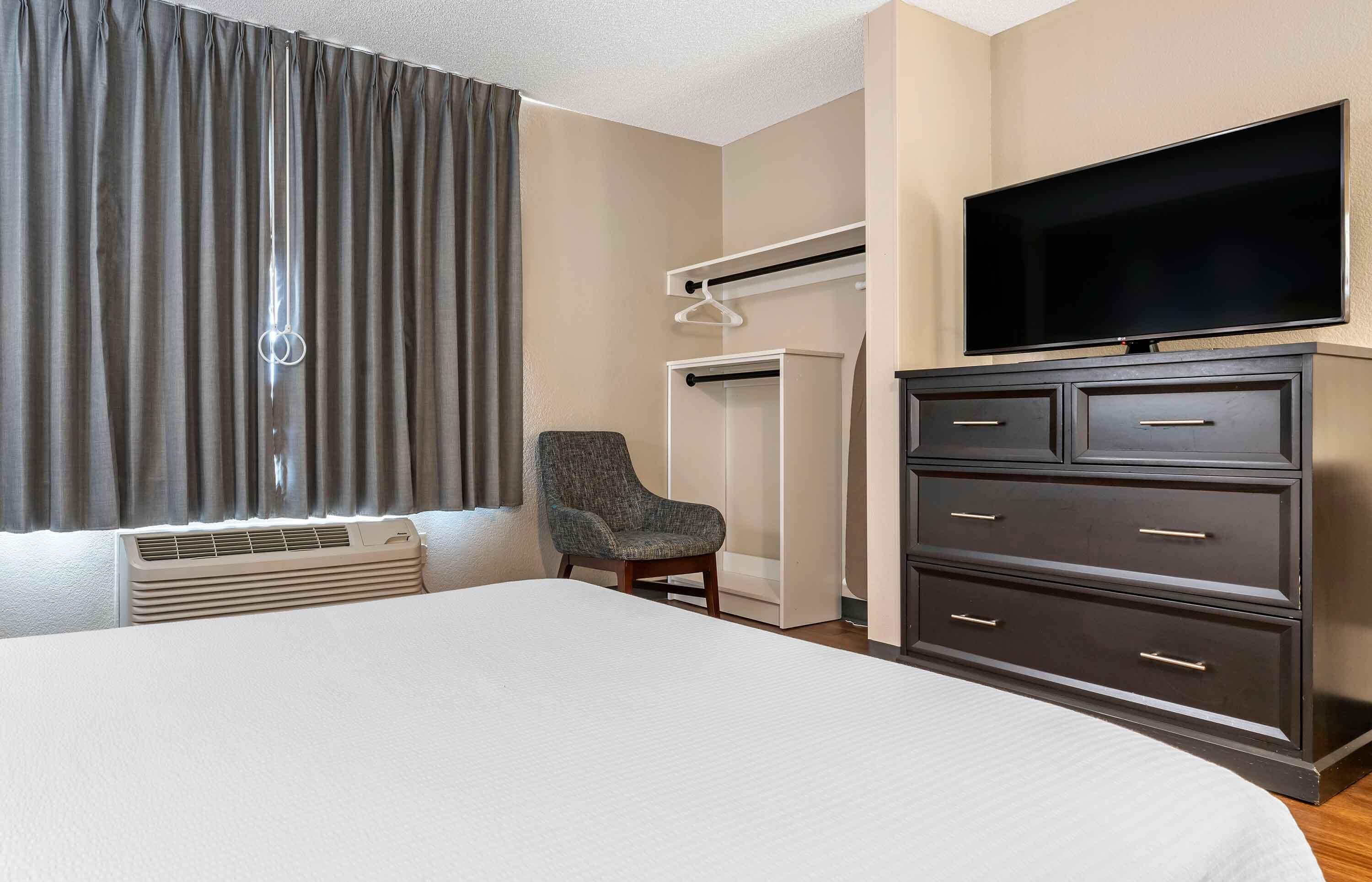 A hotel room with a large bed, a chair, a TV, a wardrobe, and a coat rack.