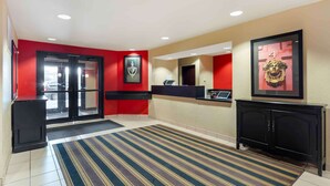Un hall d’hôtel avec un mur rouge, un comptoir d’accueil, un meuble noir et un tapis à rayures.