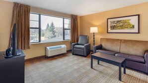 Une chambre d’hôtel avec une grande fenêtre, un canapé, un fauteuil, une table, une lampe et un téléviseur.