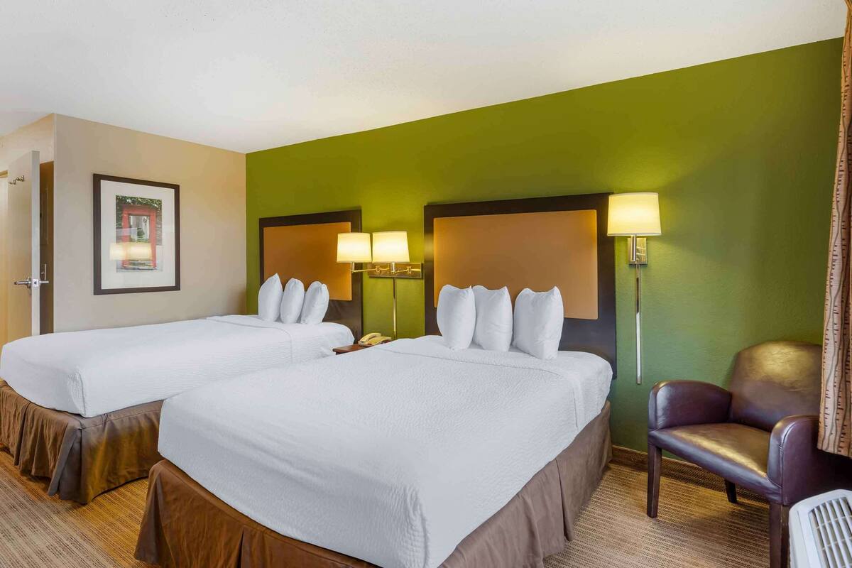 Une chambre d’hôtel avec deux lits, une chaise et une lampe.