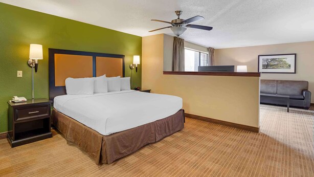 Une chambre d’hôtel comprenant un lit, des tables de chevet, un bureau, un ventilateur de plafond, un canapé et une fenêtre avec des rideaux.