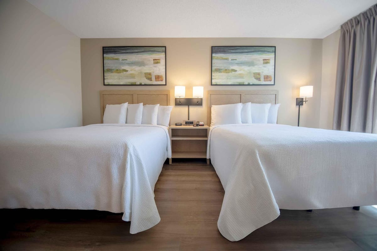 A hotel room with two beds, a nightstand, and two wall-mounted lamps.