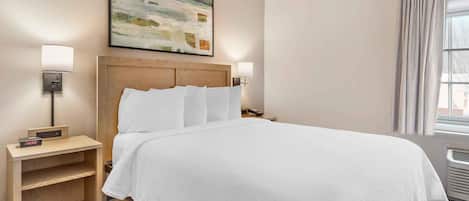 A neatly made bed with white linens, a wooden headboard, and two bedside lamps.