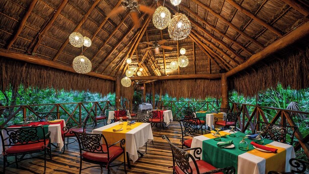 An indoor dining area with tables set for guests, a thatched roof, and hanging spherical light fixtures. - Viva Maya by Wyndham, A Trademark Resort (Playa del Carmen)