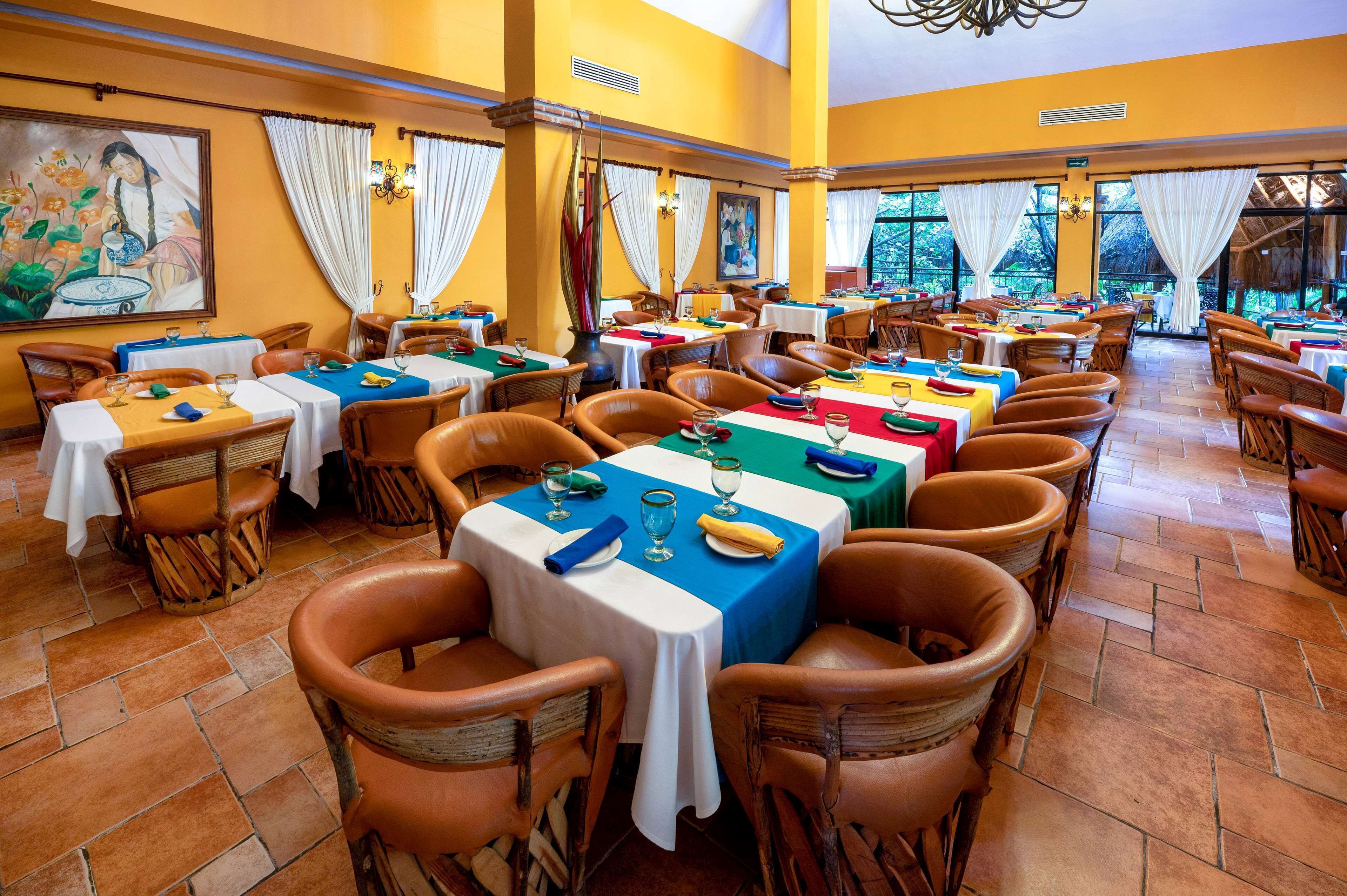 A restaurant with multiple tables and chairs, large windows, and artwork on the walls.