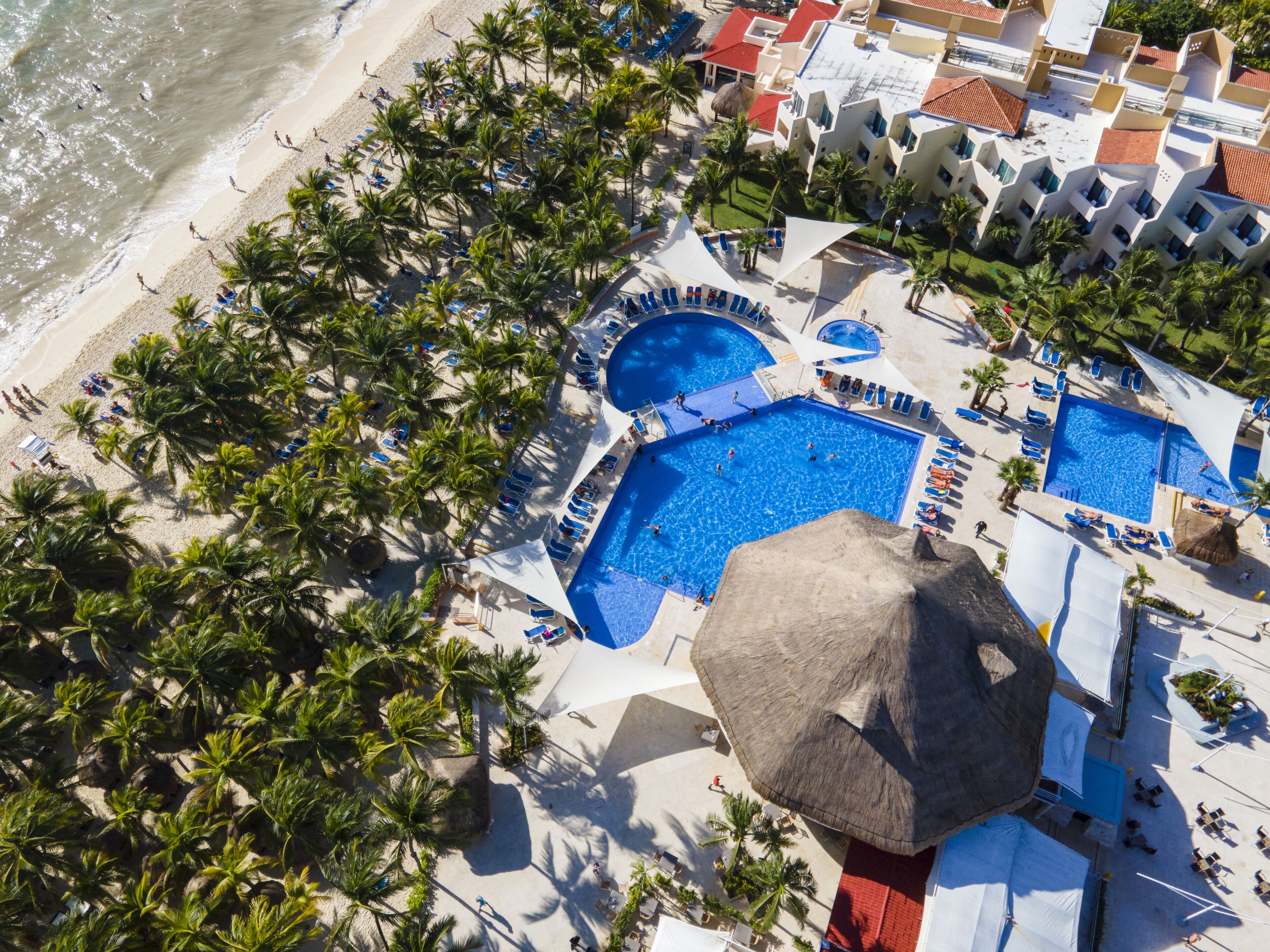 An aerial view of a resort with multiple swimming pools, palm trees, and beach access.