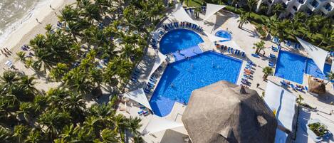 An aerial view of a resort with multiple swimming pools, palm trees, and beach access.