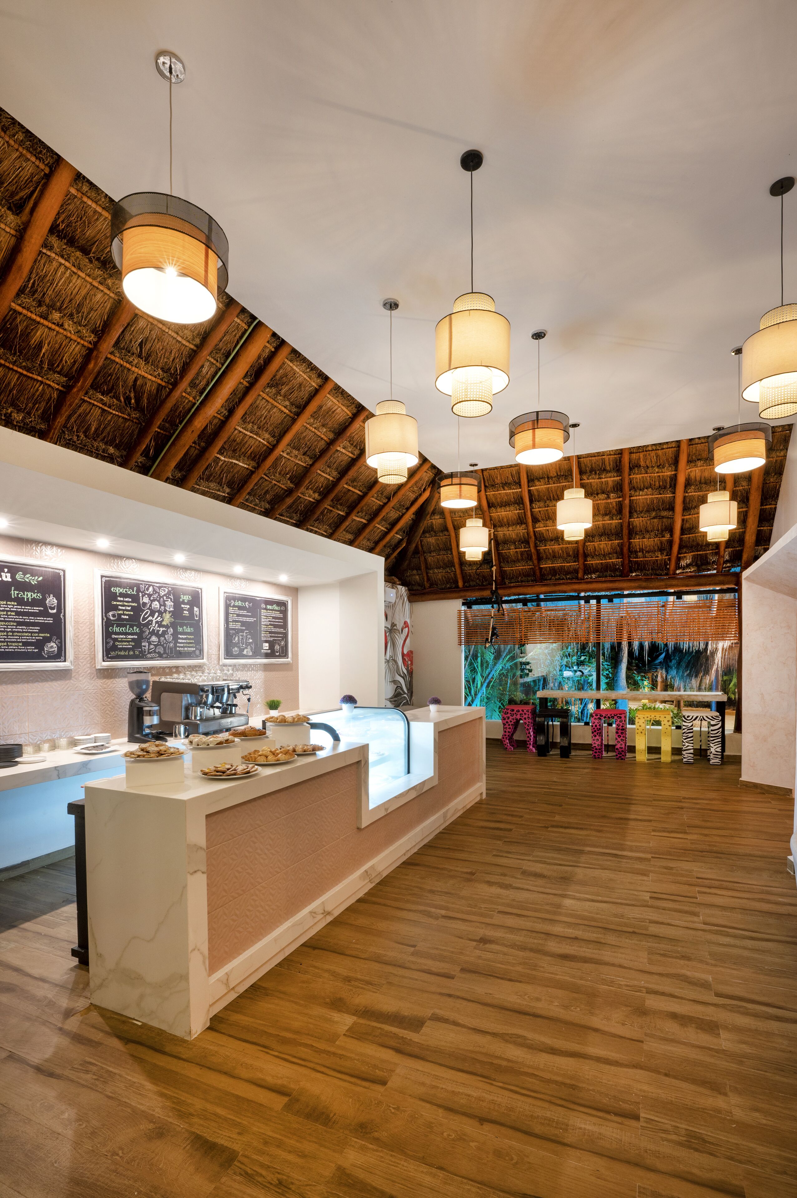 A restaurant with a high wooden ceiling, hanging pendant lights, a counter with a coffee machine, and a view of the outdoors.