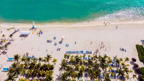An aerial view of a beach with rows of blue lounge chairs, palm trees, and a few sailboats. - Viva Maya by Wyndham, A Trademark Resort (Playa del Carmen)