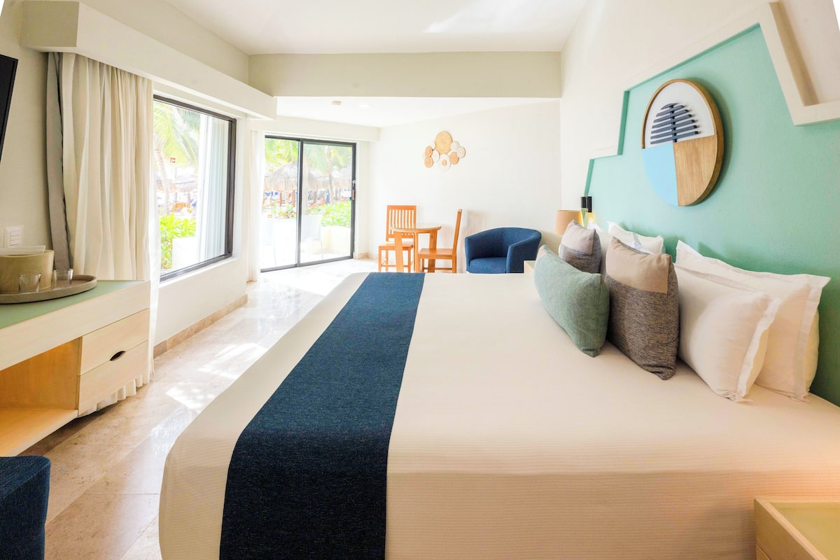 Habitación de hotel con una cama grande, un escritorio con una silla, una mesita y vistas al exterior.