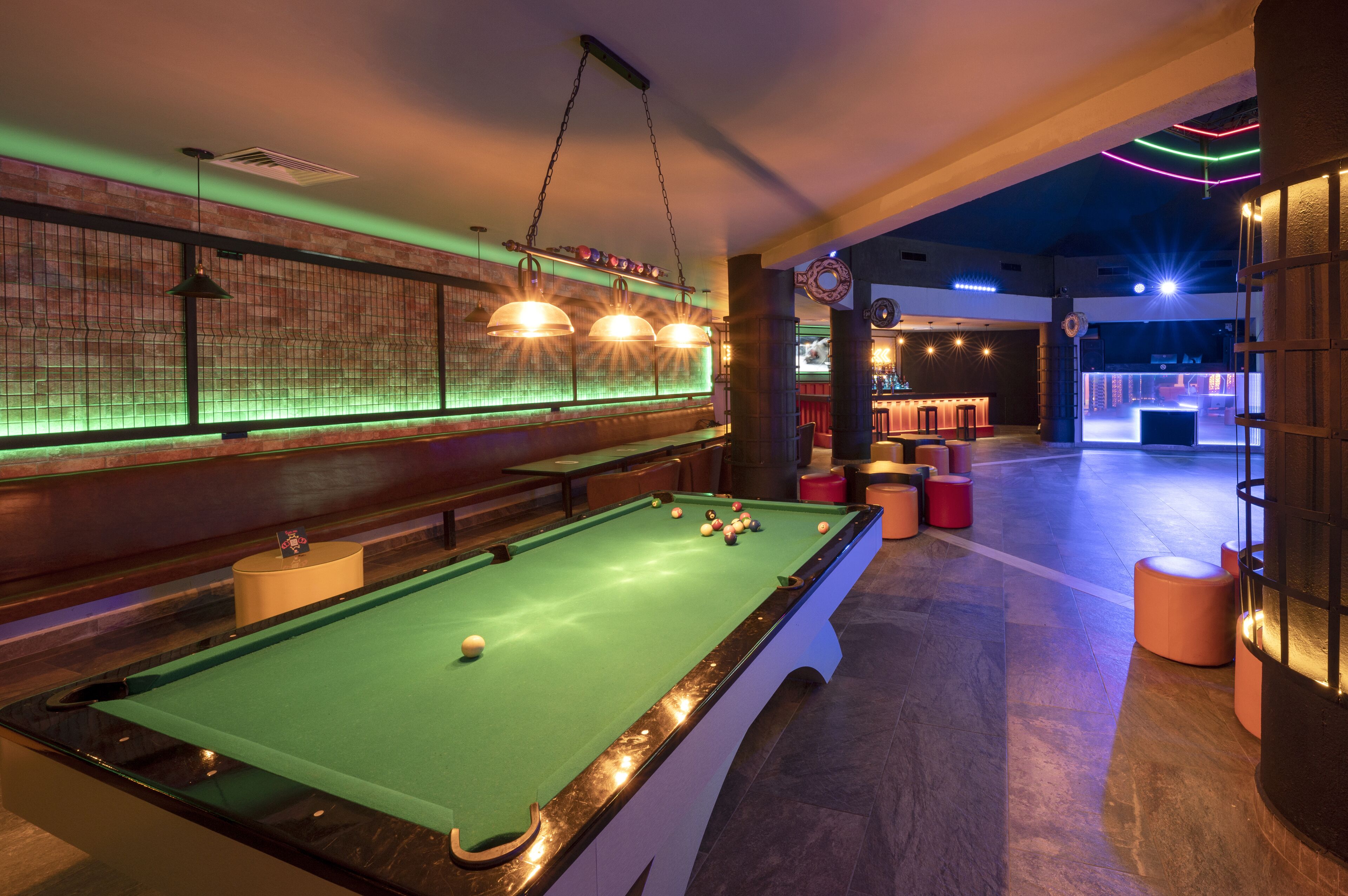 Une table de billard avec des billes, un bar et un espace détente avec des tabourets.