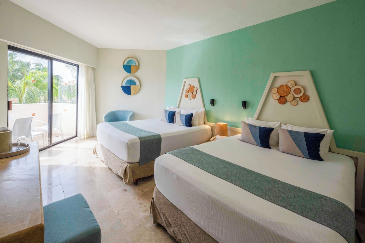 Habitación de hotel con dos camas, un balcón y vistas a palmeras.