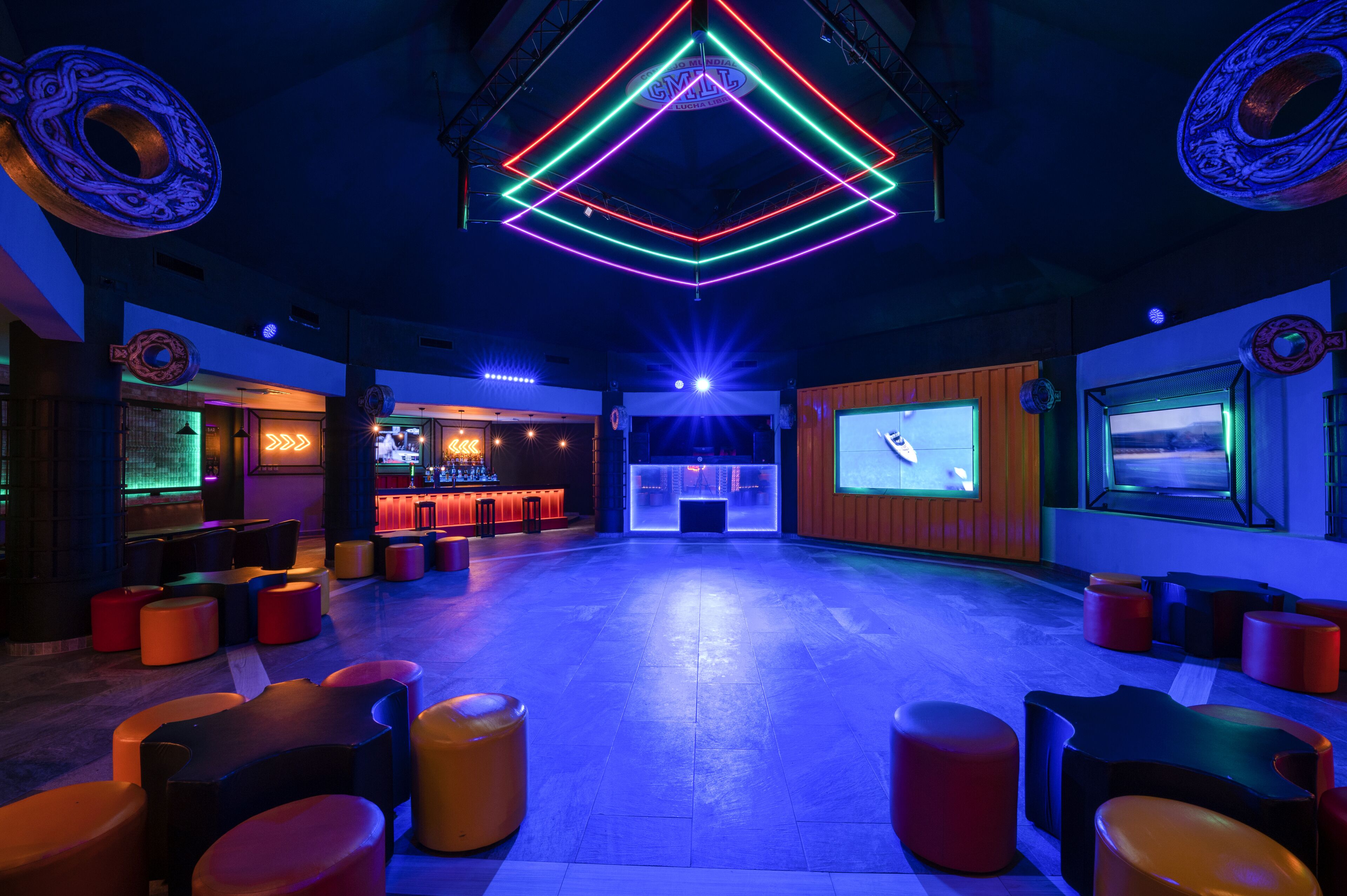 A spacious lounge area with a bar, colorful neon lights, and comfortable seating.