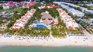 An aerial view of a resort with multiple buildings, a central pool, and a beach with sun loungers. - Viva Maya by Wyndham, A Trademark Resort (Playa del Carmen)