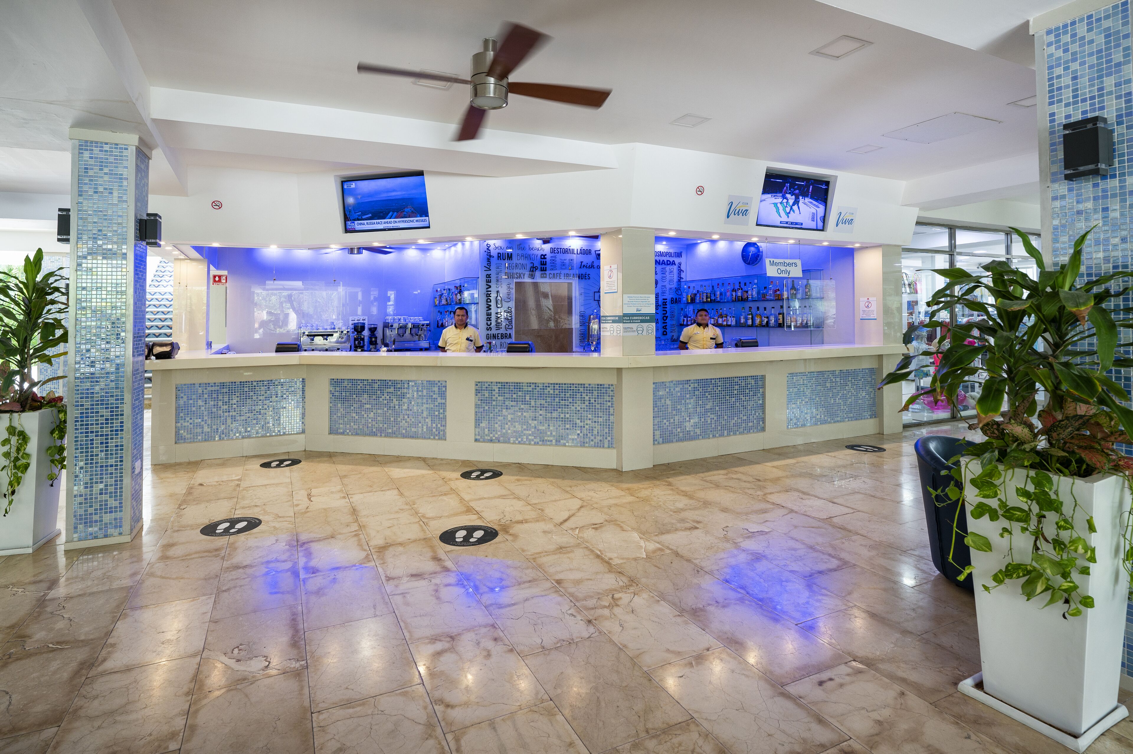 Un vestíbulo de hotel con mostrador de recepción, ventilador de techo y zona de bar.