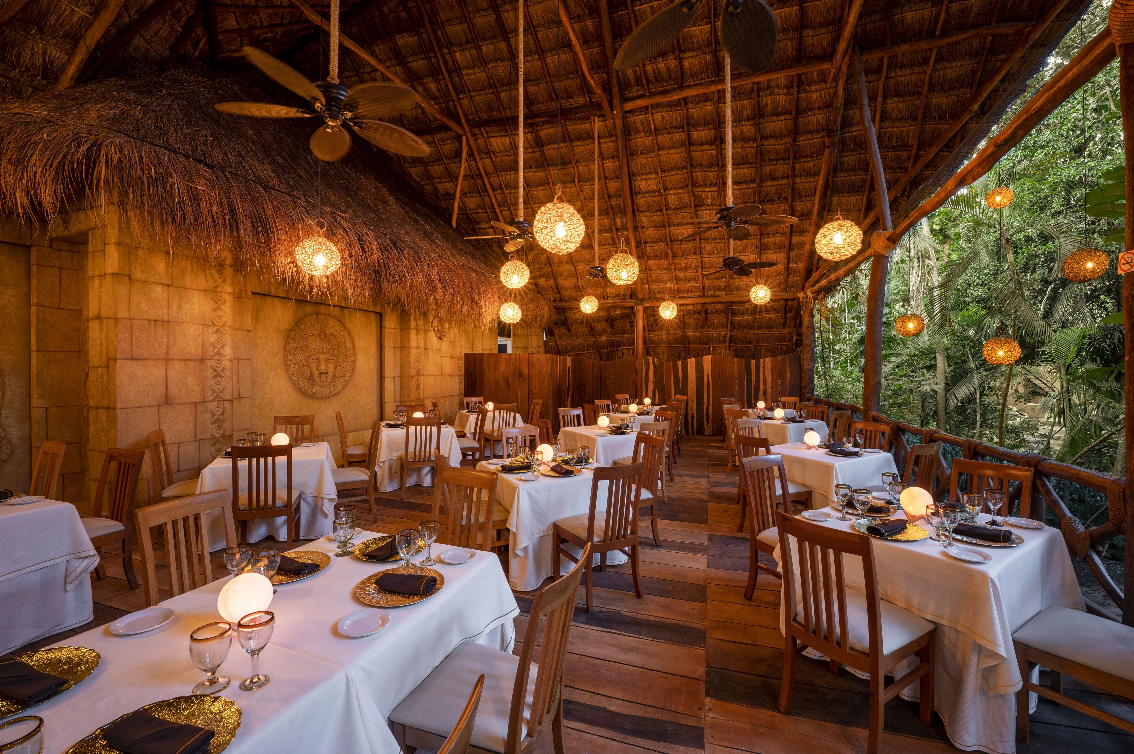 An indoor dining area with tables set for meals, wooden chairs, and hanging light fixtures.