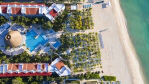 Eine Vogelperspektive zeigt ein Resort mit einem großen Pool, mehreren Liegebereichen am Strand und einer Strandlage.