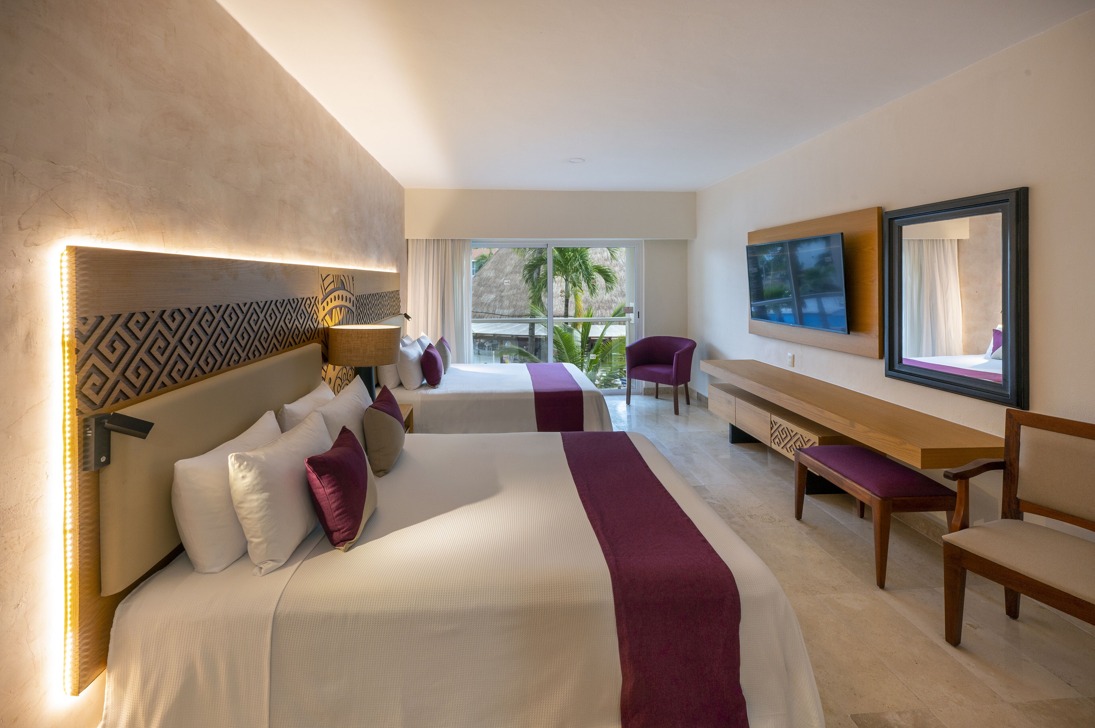 A hotel room with two beds, a bench, a chair, and a TV on the wall.