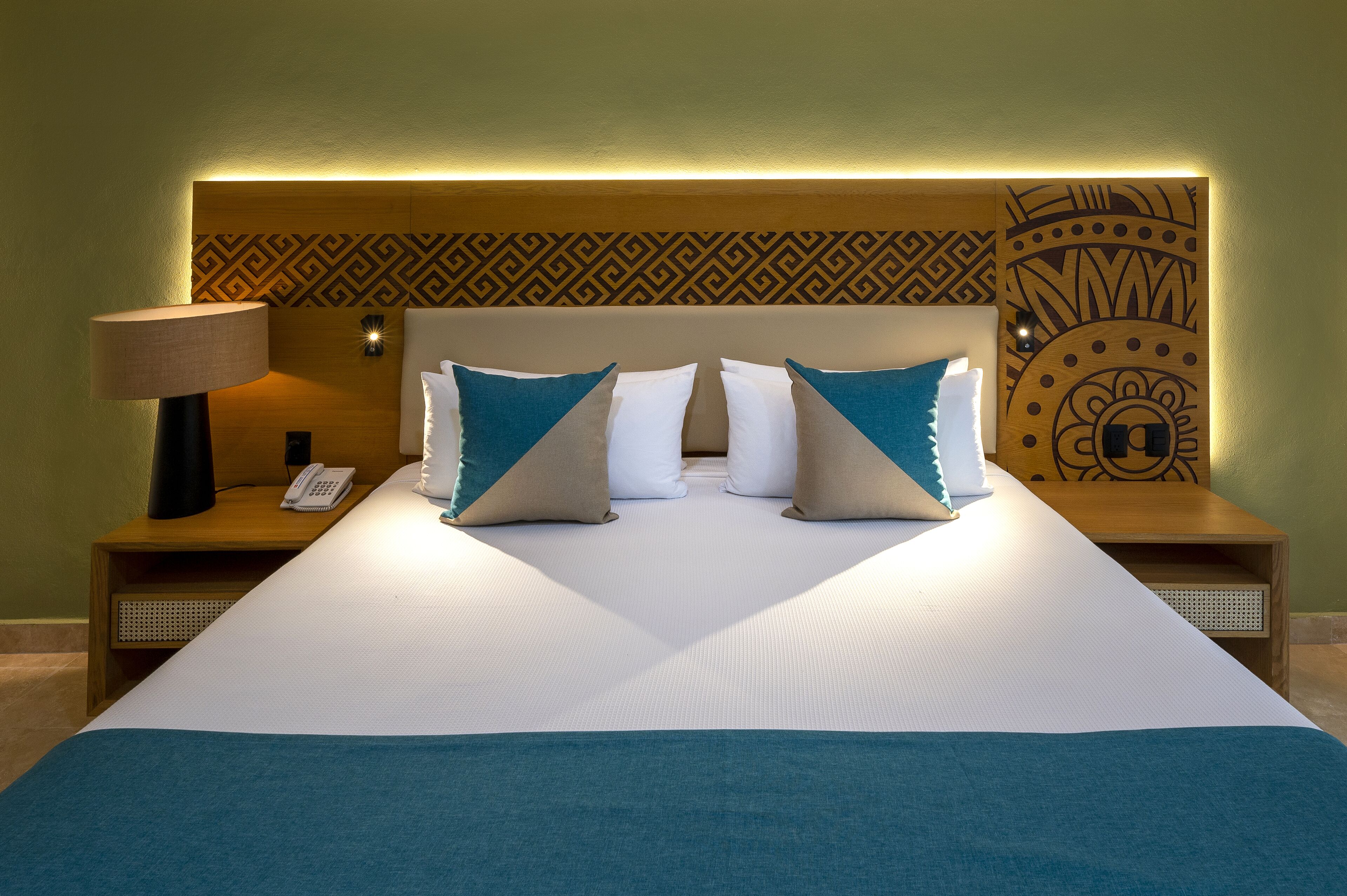 A hotel room with a large bed, two bedside tables, a lamp, a phone, and a decorative headboard.