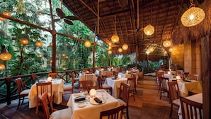 An outdoor dining area with tables set for guests, surrounded by lush greenery and a thatched roof structure. - Viva Azteca by Wyndham, A Trademark  Resort (Playa del Carmen)