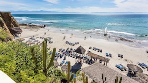 Una playa con construcciones de techo de paja, sillas de descanso y una vista despejada del océano.