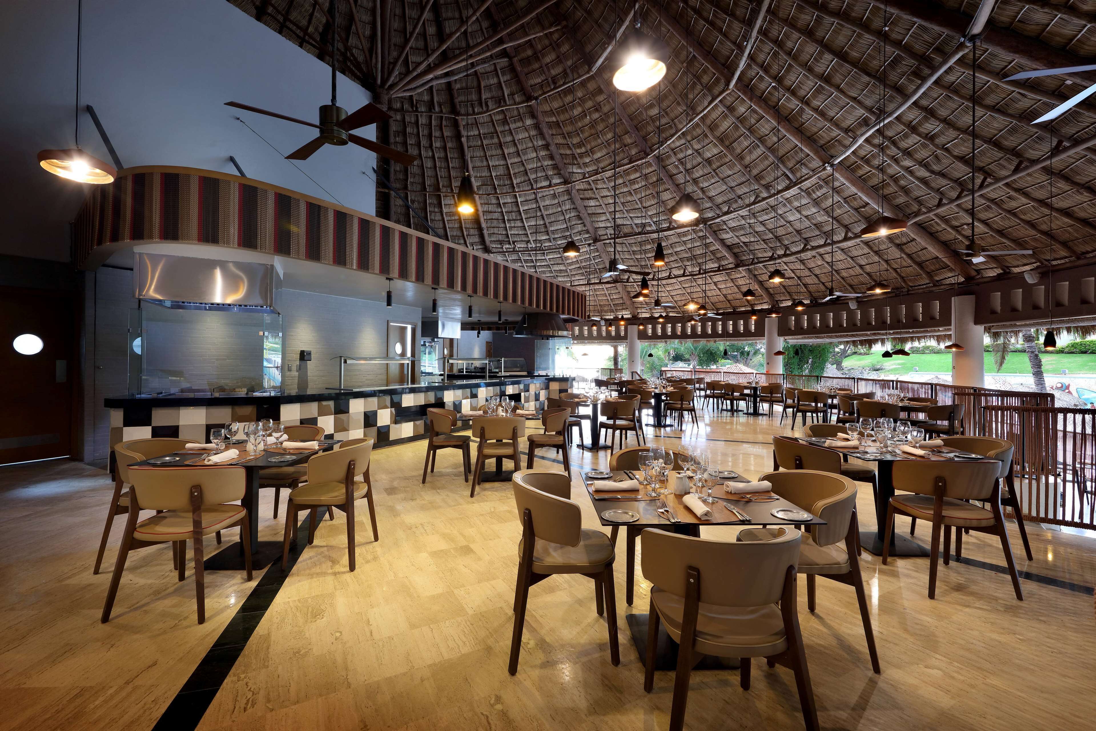 Un restaurante espacioso con techos altos, una zona de bar central y numerosas mesas y sillas.