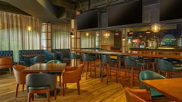 Un área de bar moderna con mesas y sillas de madera, un televisor de pantalla plana grande y una barra con un letrero de neón.