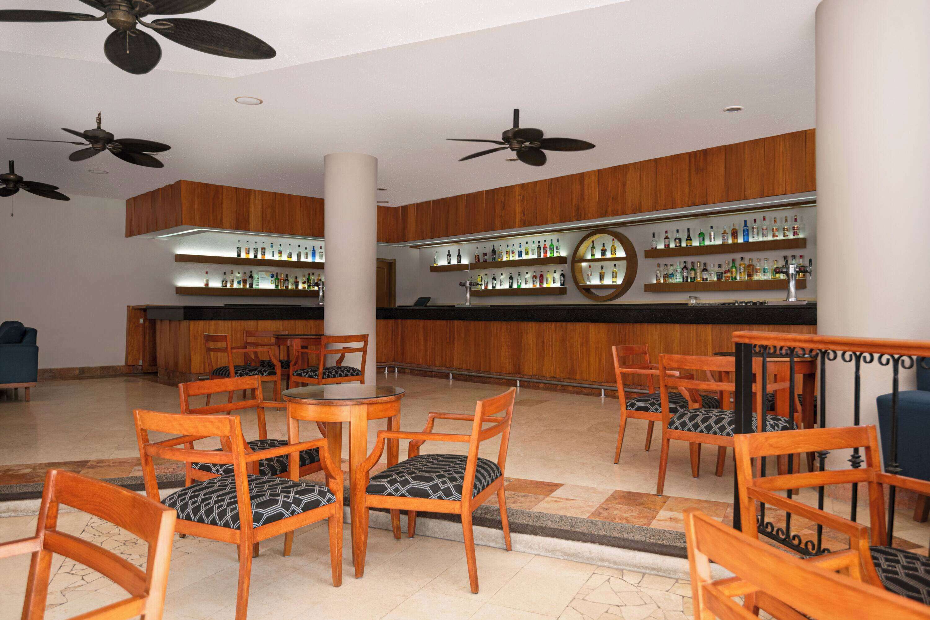 A lobby with wooden furniture, a bar area with shelves of bottles, and ceiling fans.