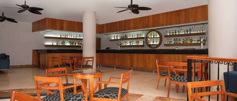 A lobby with wooden furniture, a bar area with shelves of bottles, and ceiling fans.