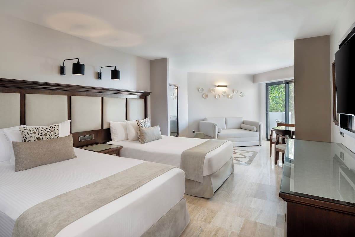 A hotel room with two beds, a TV, a sofa, and a dining area.