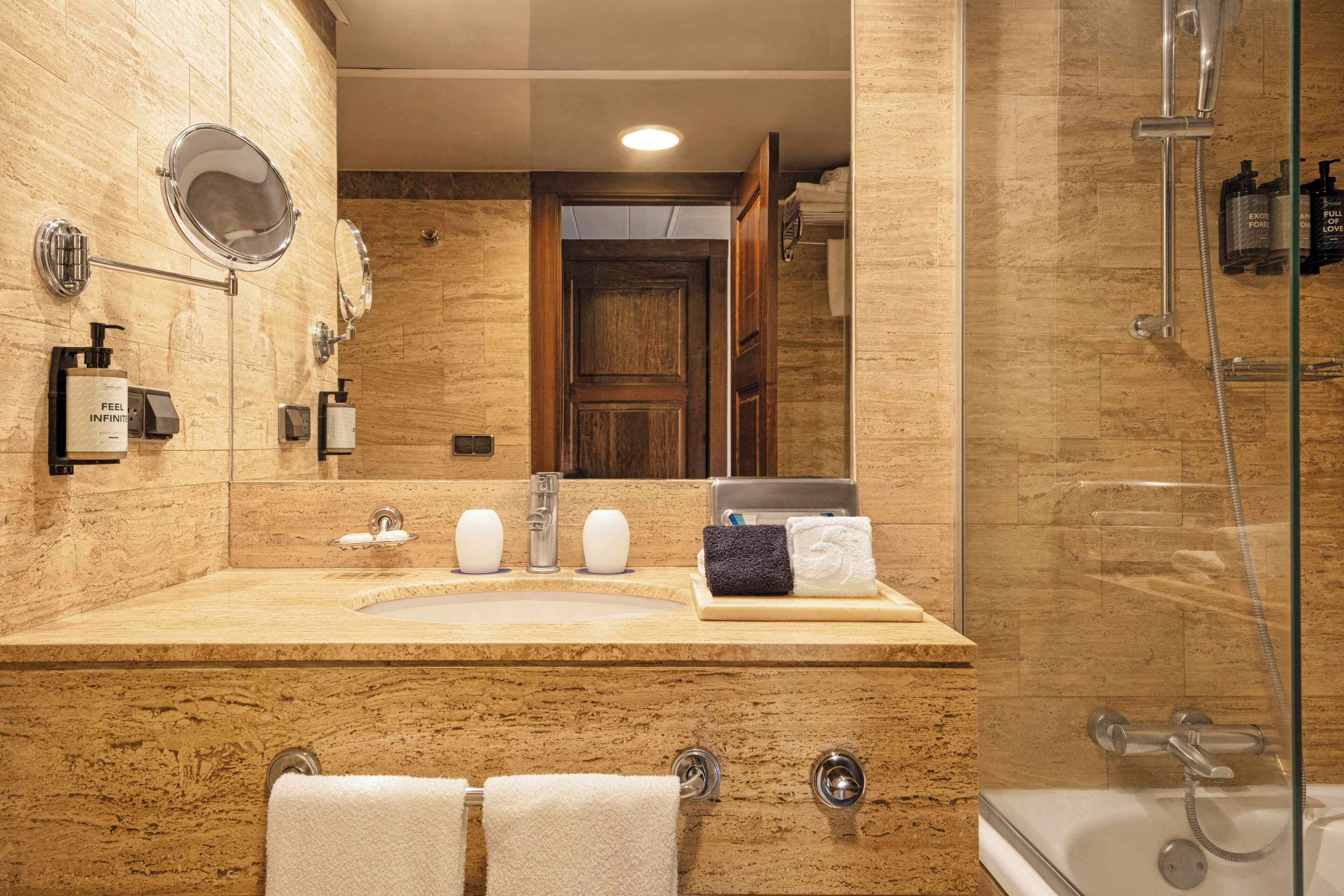 Une salle de bain avec un meuble-lavabo en marbre, un grand miroir, un lavabo et un espace douche.